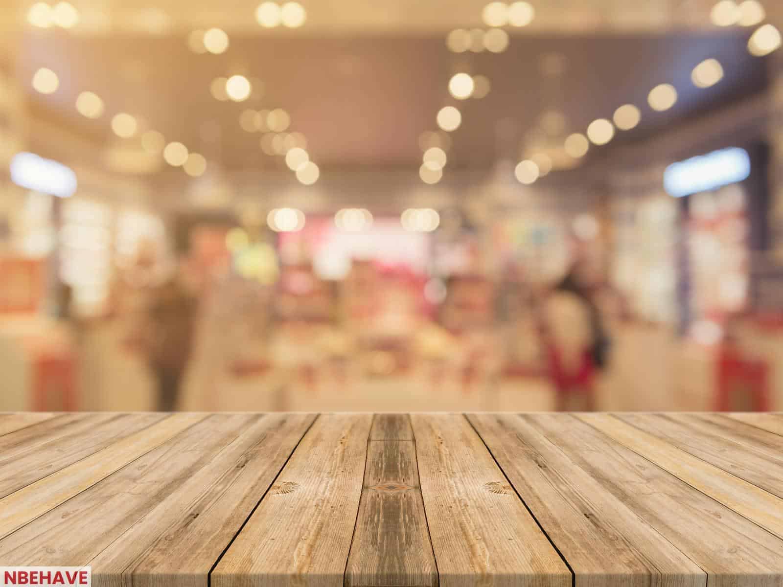 Empty wooden table with blurred shopping mall background and bokeh lights.
